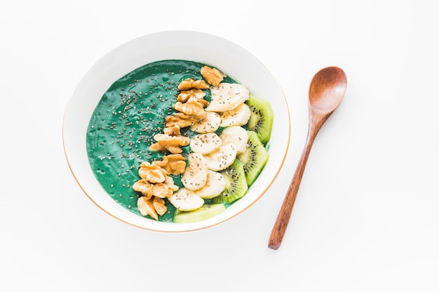 Spirulina smoothie bowl with banana, walnuts, kiwi and chia seeds on white