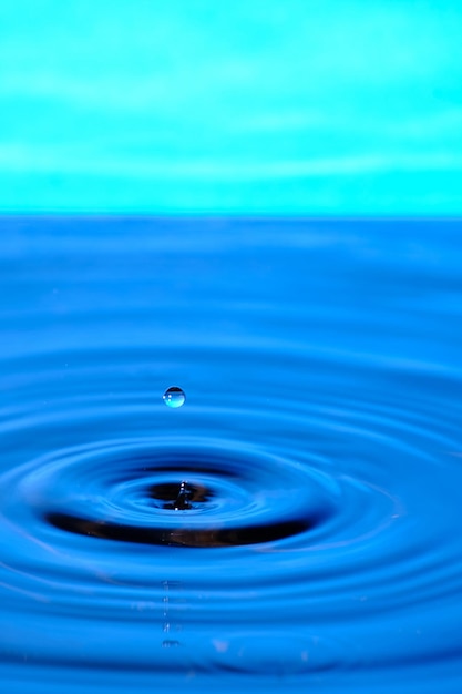 Splash drop of water with diverging water circles on blue background