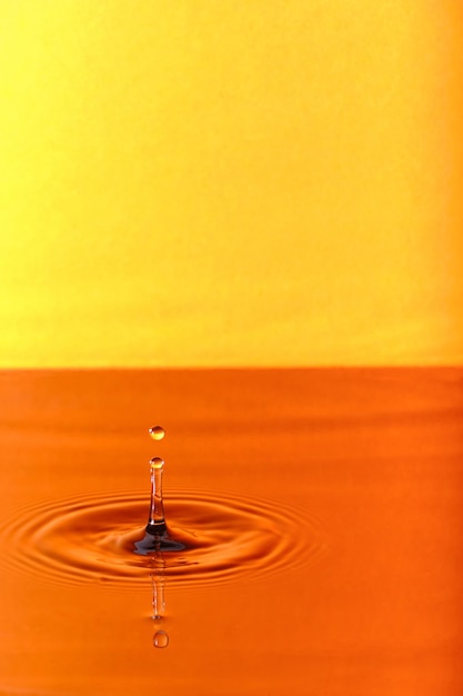 Splash drop of water with diverging water circles on orange background