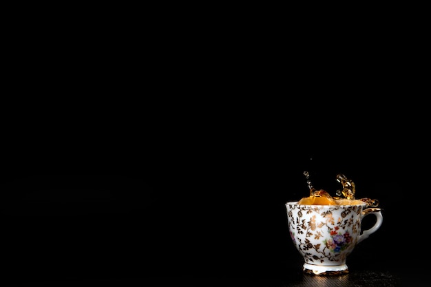 Splash in vintage cup of black tea isolated on black background with delicious cookies copy space de