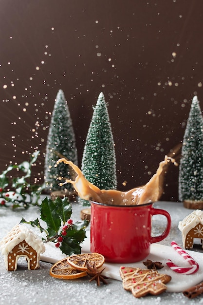 Splashes of Christmas cappuccino in red mug on grey table with gingerbread cookies.