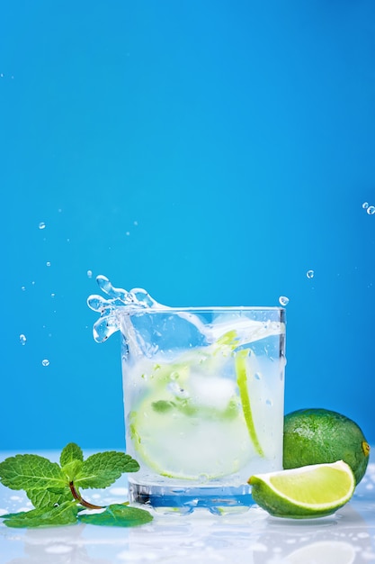 Splashing mojito cocktail with lime and fresh mint in glass on a blue background