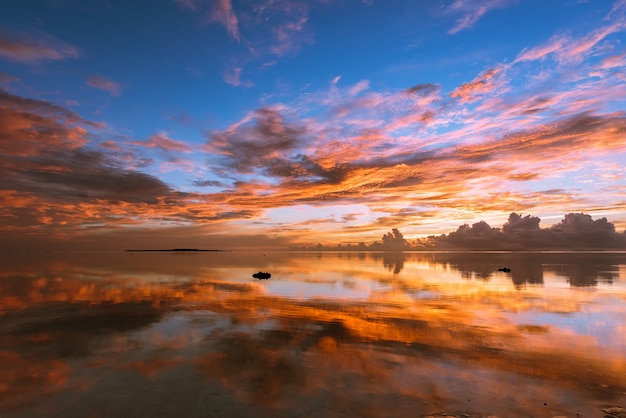 Splendid colorful sunrise, yellow, orange, pink and blue clouds reflecting on the smooth surface sea like a mirror.