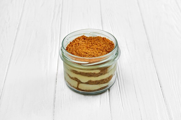 Sponge cake with cream in a jar on a white wooden background