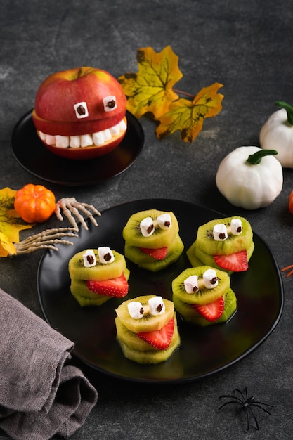 Spooky green kiwi monsters for Halloween Healthy Fruit Halloween Treats Halloween party kiwi strawberry apple and marshmallow monster on dark grey stone or concrete table background