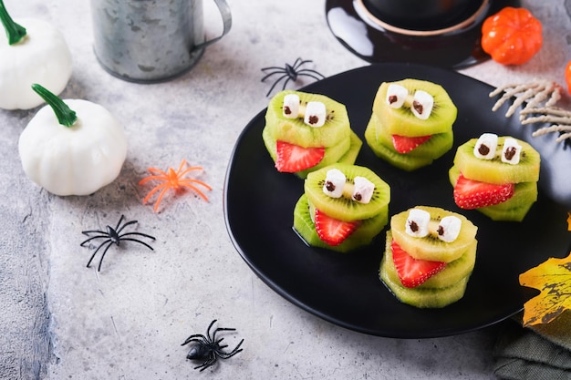 Spooky green kiwi monsters for Halloween Healthy Fruit Halloween Treats Halloween party kiwi strawberry apple and marshmallow monster on grey stone or concrete table background Selective focus