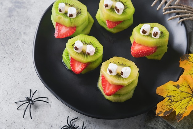 Spooky green kiwi monsters for Halloween Healthy Fruit Halloween Treats Halloween party kiwi strawberry apple and marshmallow monster on grey stone or concrete table background Selective focus