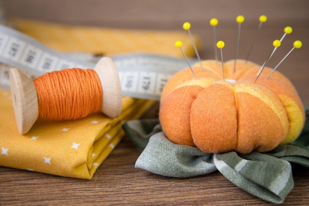 A spool of thread cotton fabric needles and a needle holder on a wooden table Sewing Accessories