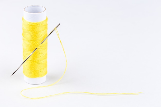 Spool of yellow threads and a needle on white background