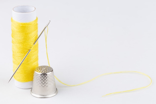 Spool of yellow threads and a needle on white background