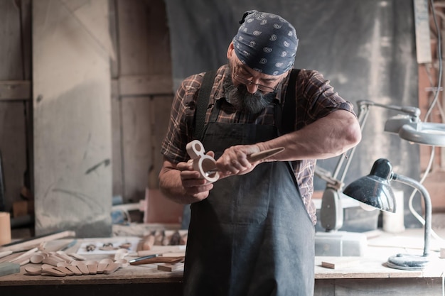 Spoon craft master in his workshop with handmade wooden products and tools working checking curve and line straight. High quality photo