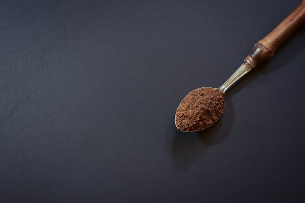 Spoon filled with coffee powder on black background.