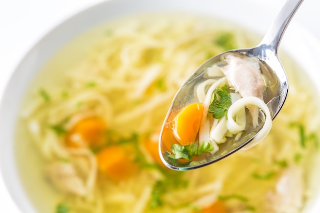 Spoon full of chicken or beef soup with noodles carrot and herbs.