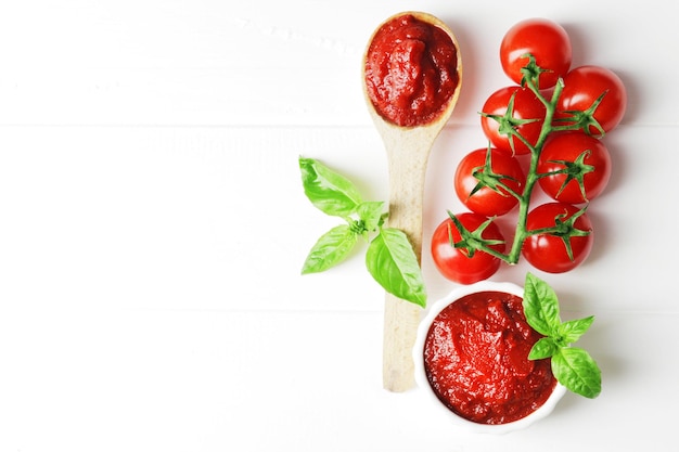 A spoon full of tomato sauce on a white wooden background with ingredients