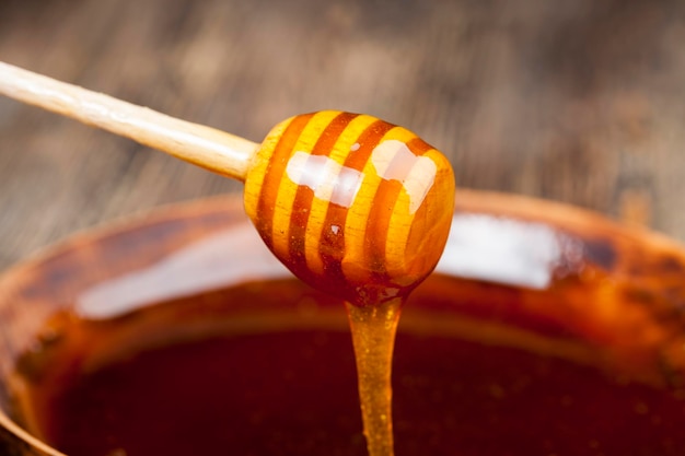 A spoon for honey together with high-quality bee honey, an old table on which there is a healthy and sweet bee honey and a homemade wooden spoon that allows you to transfer and pour honey