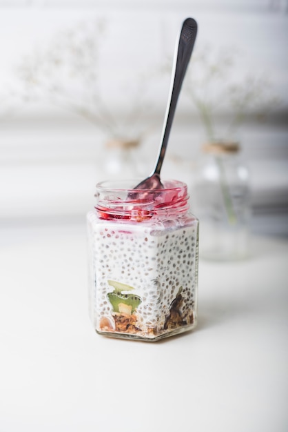 Spoon inserted in transparent glass jar on white backdrop