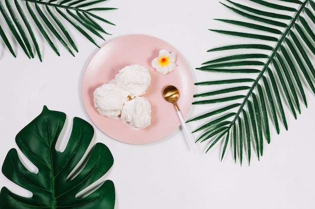 Spoon near ice cream on plate between plants