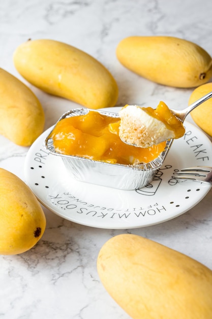 Spoon scooped up the mango cheese pie Mango Cheese Pie is packaged in a square aluminum foil in a white plate on a marble table cake in cafe or bakery shop