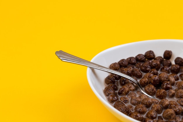 Spoon in White bowl with chocolate corn cereal balls and milk on yellow