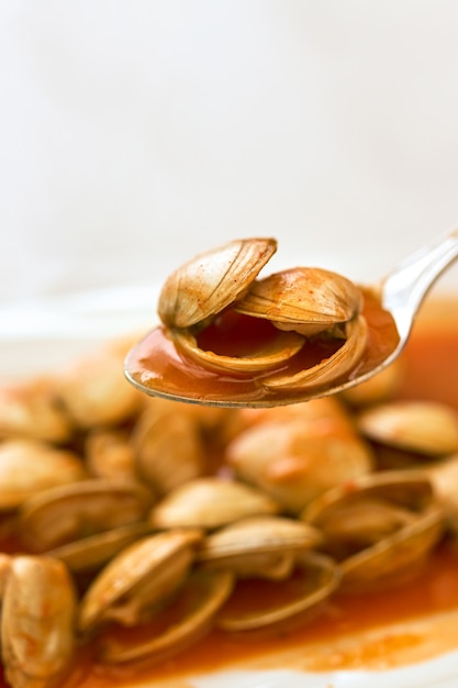 Spoon with clams in sauce on a plate of clams.