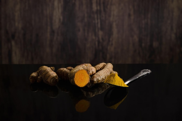 Spoon with curcuma and turmeric roots on black table with wood background