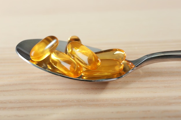 Spoon with fish oil capsules on wooden table