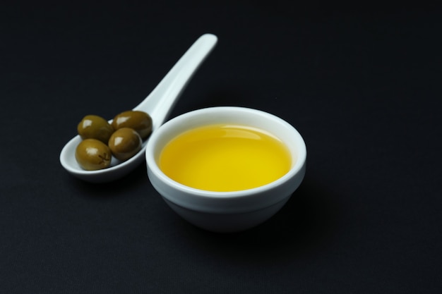 Spoon with olives and bowl of oil on black