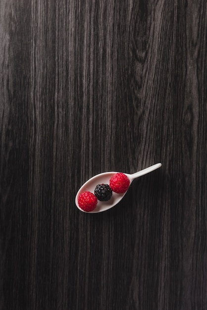 Spoon with raspberry and blackberries background black wood