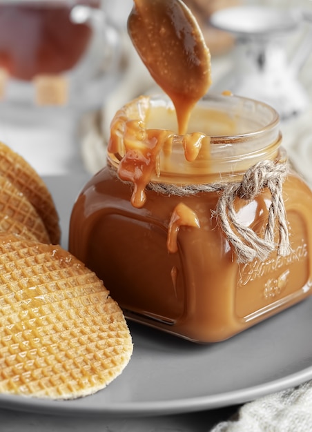 Spoon with tasty caramel sauce over jar on table.