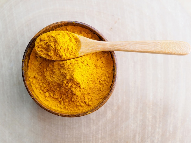 Above of spoon with yellow turmeric powder in wooden bowl on wood board.