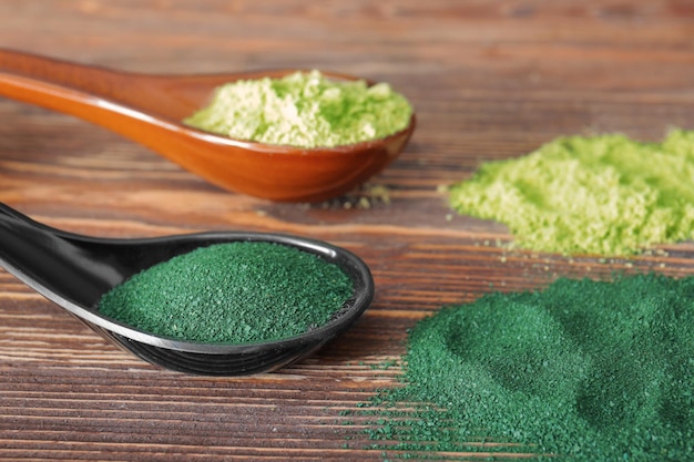 Spoons with spirulina and wheat grass powder on wooden background