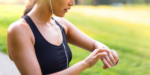 Sport asian woman listening to music with headphones while looking at watch outdoors