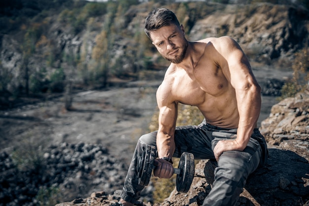 Sport, bodybuilding, lifestyle and people concept - young man with barbell flexing muscles. Fitness man having workout outdoor.