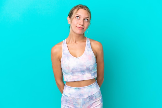 Sport caucasian woman isolated on blue background and looking up