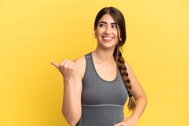 Sport caucasian woman isolated on yellow background pointing to the side to present a product