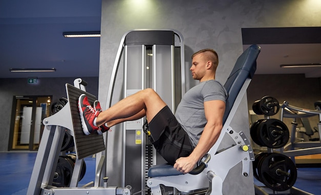 sport, fitness, bodybuilding, lifestyle and people concept - man exercising and flexing leg muscles on gym machine