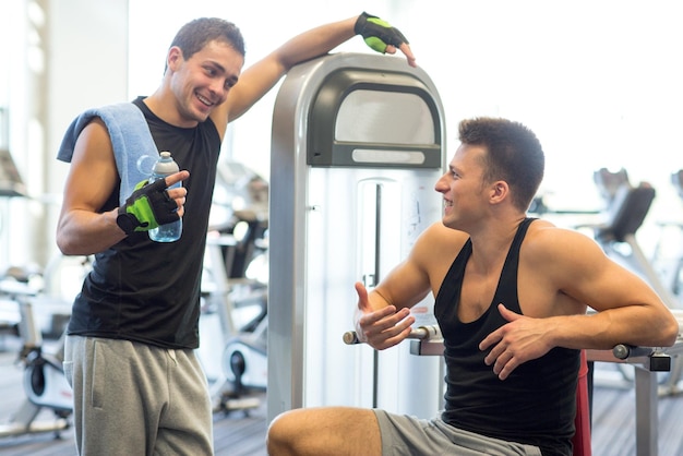 sport, fitness, equipment, lifestyle and people concept - smiling men with bottle of water exercising on gym machine