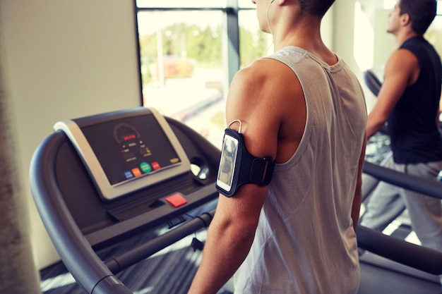 sport, fitness, lifestyle, technology and people concept - smiling men exercising on treadmill in gym