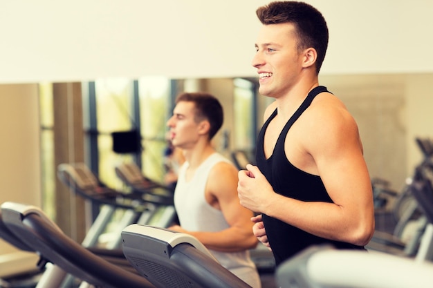 sport, fitness, lifestyle, technology and people concept - smiling men exercising on treadmill in gym