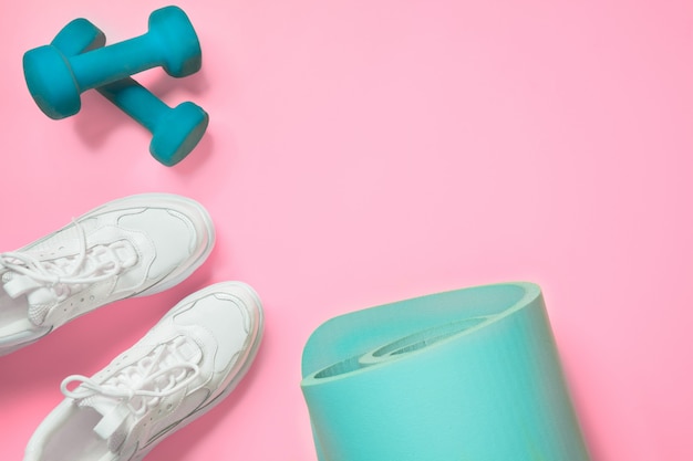 Sport and fitness shoes, dumbbell, yoga mat on pink. 