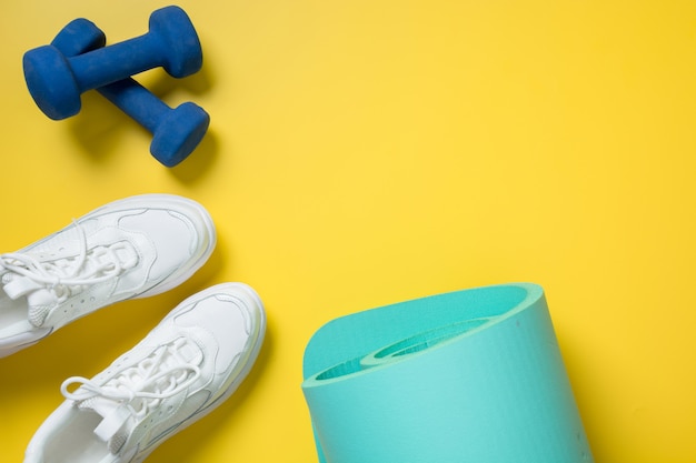 Sport and fitness shoes, dumbbell, yoga mat on yellow. Space for text.