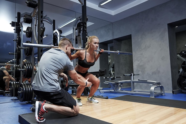 sport, fitness, teamwork, bodybuilding and people concept - young woman and personal trainer with bar flexing muscles in gym