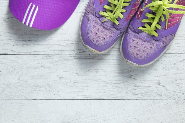 Sport flat lay purple shoes and cap on white wooden background. 