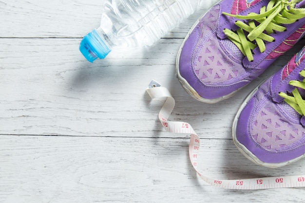 Sport flat lay purple shoes and measuring tape on white wooden background.