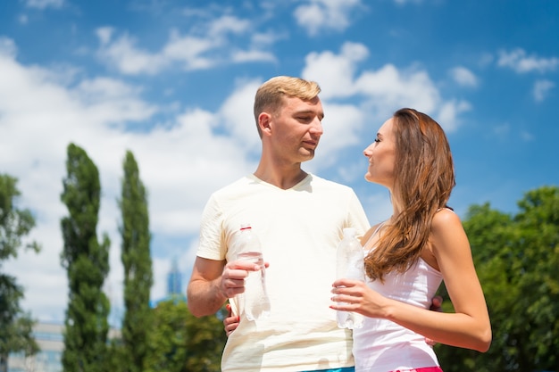 Sport and health. Woman and man drink water from bottle. Summer activity and energy. Girl and guy sunny outdoor. Couple of coach relax after workout.