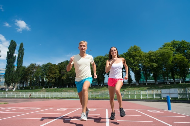 Sport and healthy fitness. Couple running on arena track. Man and woman sunny outdoor on blue sky. Coach and trainer at workout. Runner on competition and future success.