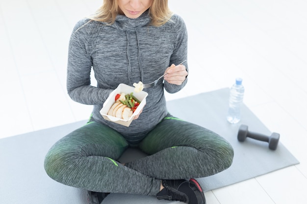 Sport, healthy, people concept - Close-up of girl holding salad and dumbbell after fitness training