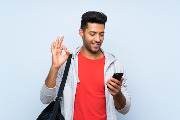 Sport man over isolated blue wall showing ok sign with fingers