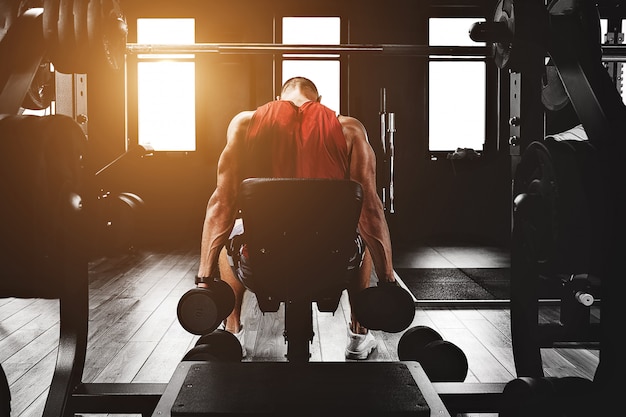 Sport motivation. gym theater. Muscular guy bodybuilder doing exercises with dumbbells in the gym. Athletic body, healthy lifestyle, fitness motivation, body positive.