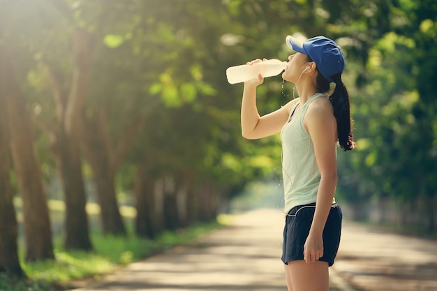 Sport runner girl drinking fresh water after running in the park.